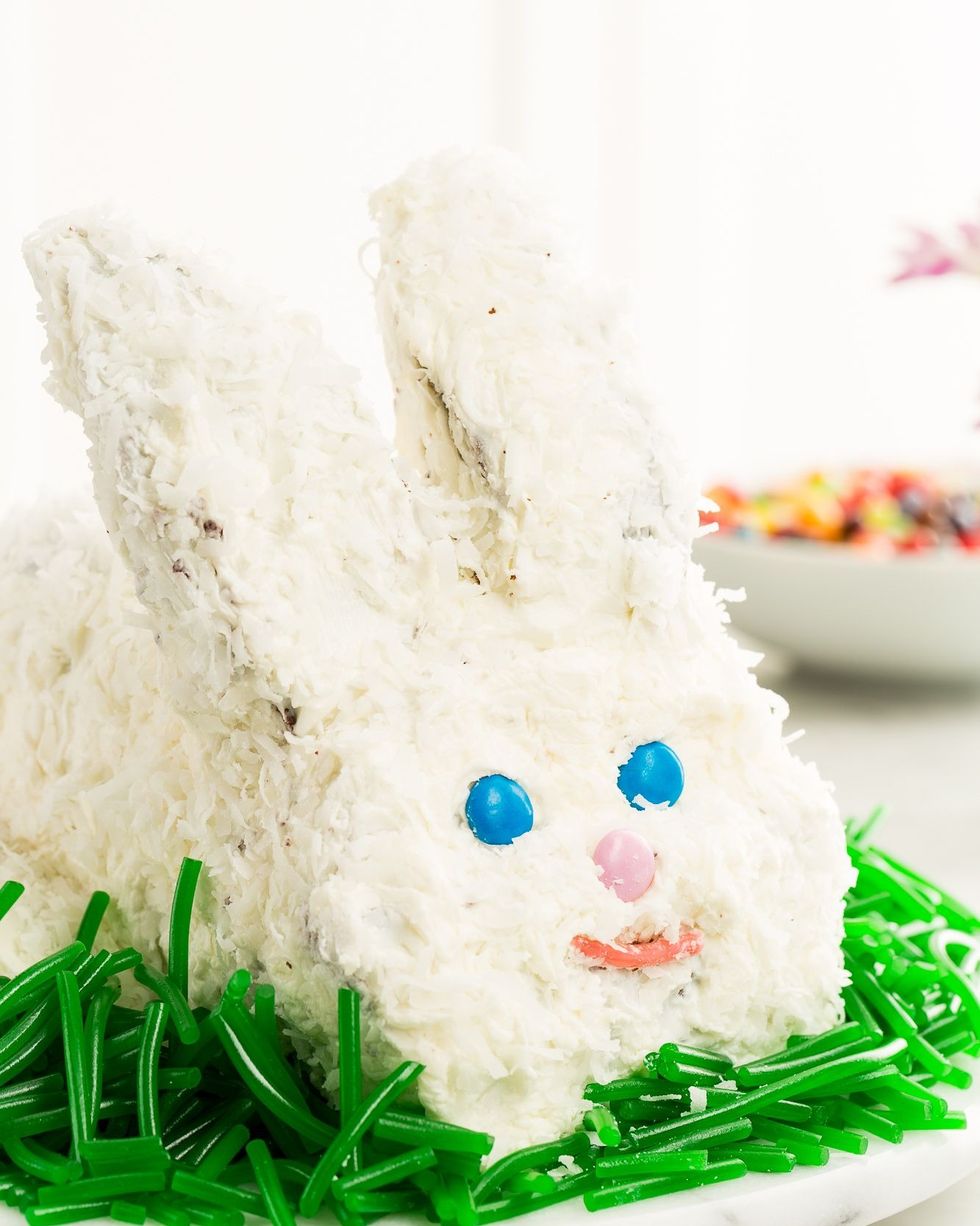 easy easter bunny cake covered in shredded coconut with blue candy eyes a pink candy nose and a red candy smile