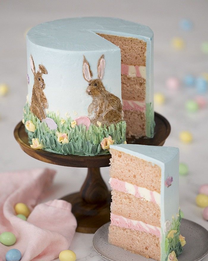 a layer cake with easter bunnies gras and flowers painted with frosting aroundt he outside