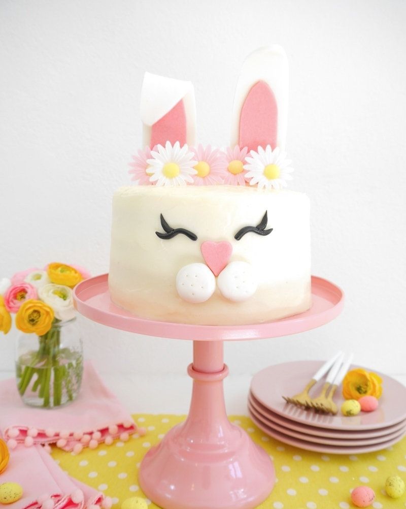 vanilla cake with a bunny face on the side and two ears coming out of the top with a white and pink daisy flower crown