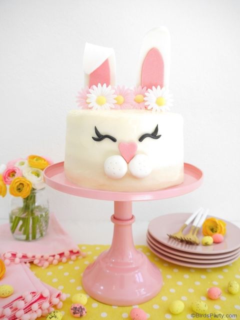 vanilla cake with a bunny face on the side and two ears coming out of the top with a white and pink daisy flower crown