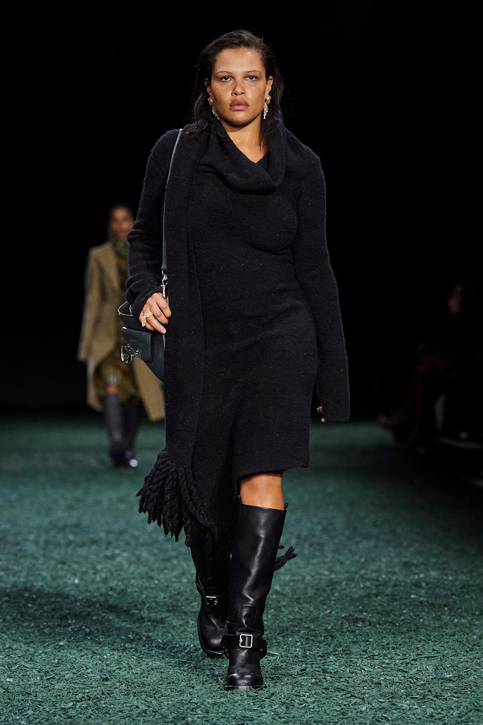 Fashion model walking on a runway wearing a black outfit and tall boots