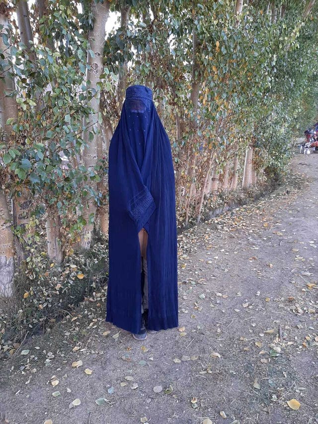 a woman in a long blue burqa stands on a dirt path