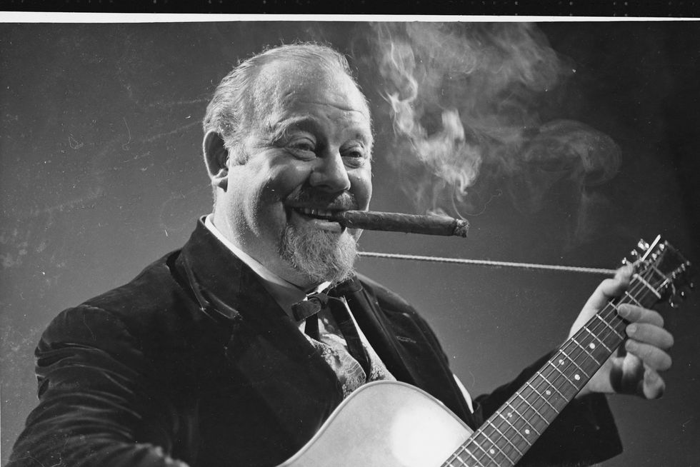 burl ives smokes a cigar while playing guitar