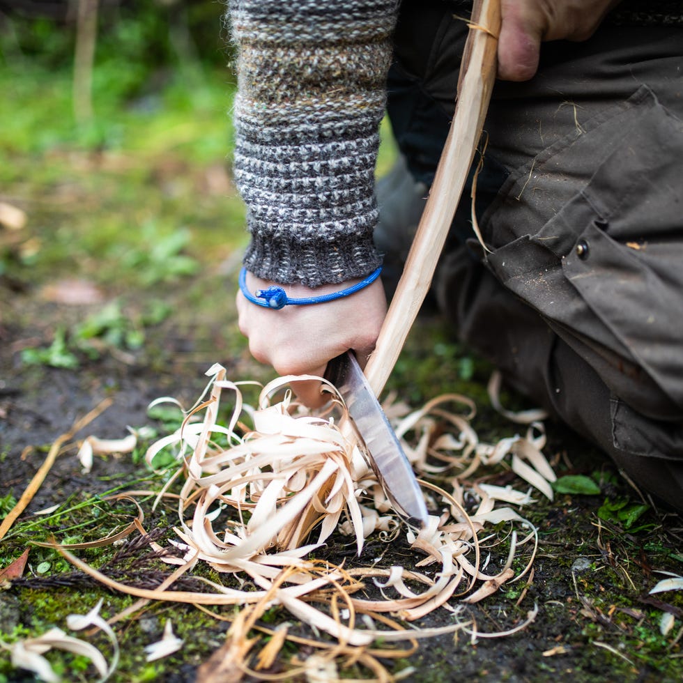 a close up of a man carving off tinder with a knife for a fire