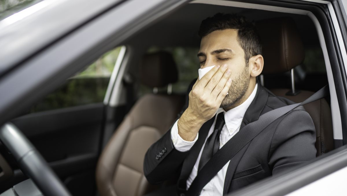 Businessman blowing his nose inside the car