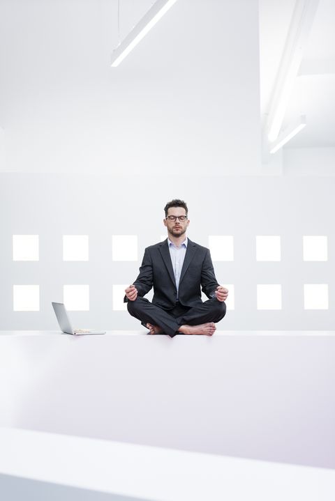 Businessman doing yoga in office next to laptop