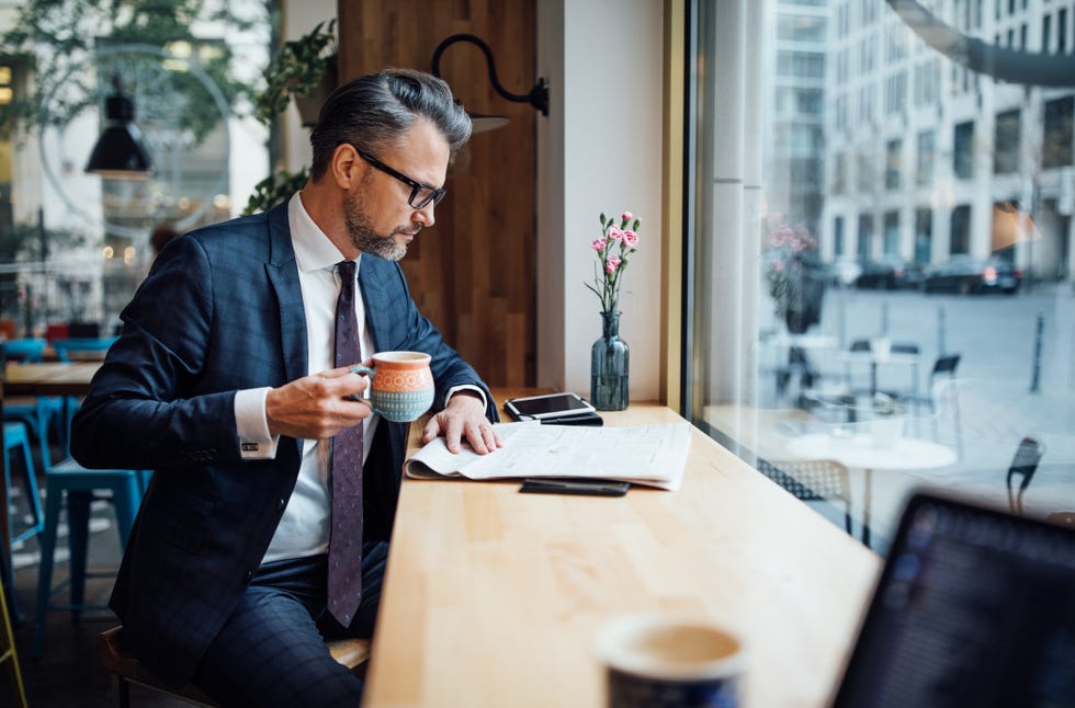 Businessman drinking coffee and reading newspaper at cafe