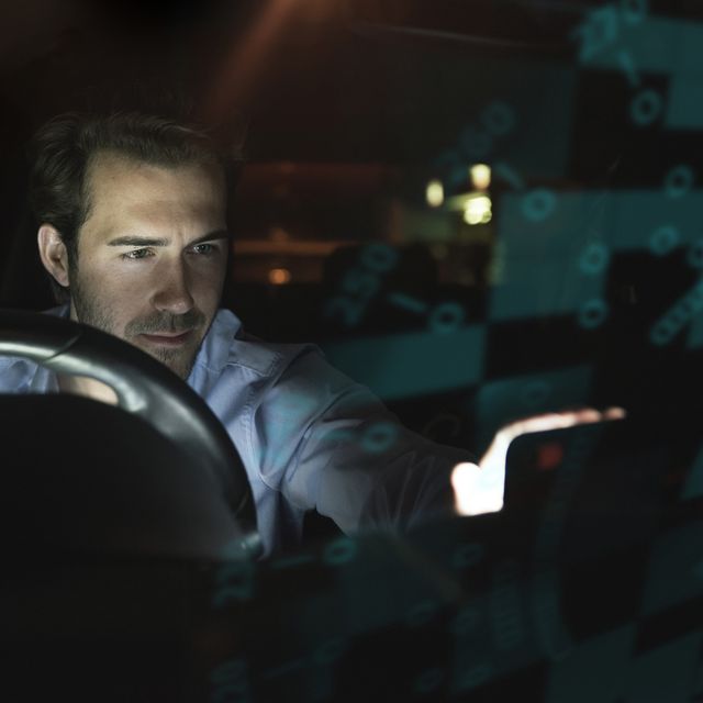 Businessman using device in car at night surrounded by data