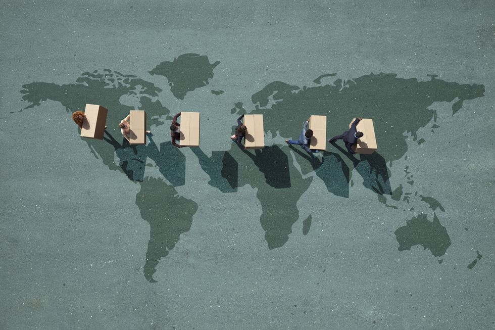 businesspeople walking across painted world map, carrying moving boxes