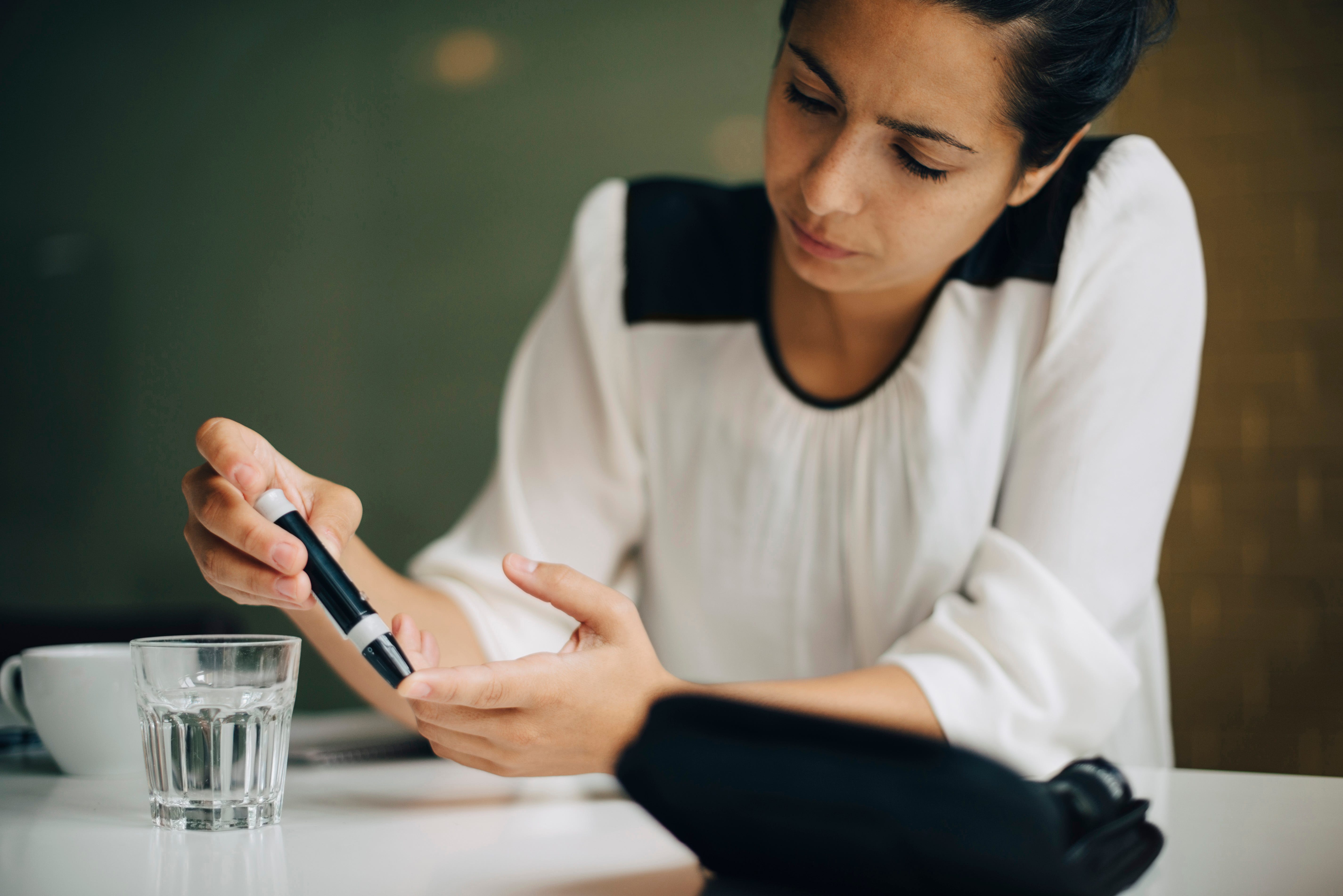 businesswoman checking blood sugar level with diabetes kit at table