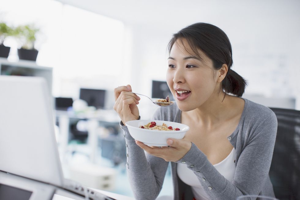 Businesswoman eating cereal and looking at laptop in office