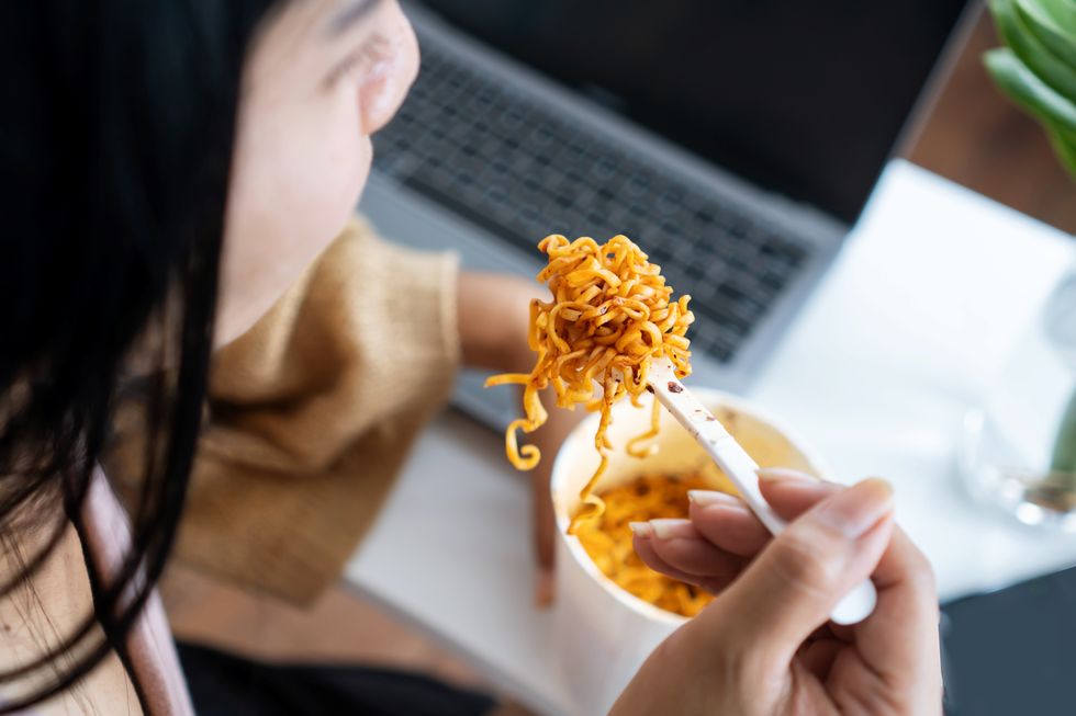 businesswoman eating spicy noodles at workplace sitting at the office with notebook on desk