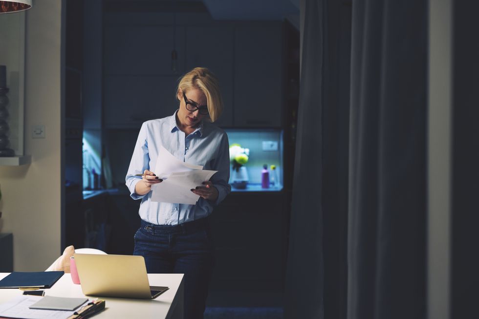 businesswoman reading documents while standing by desk in home office