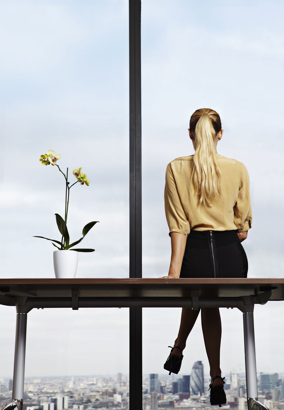 Businesswoman sitting on desk looking out window
