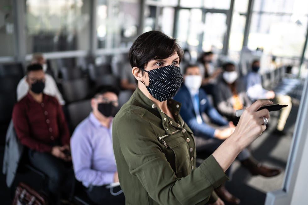 mujer de mediana edad con mascarilla escribe en una pizarra con rotulador