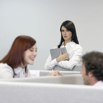 businesswoman watching two coworkers talking over cubicle wall