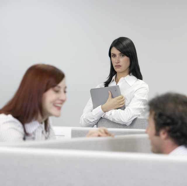 businesswoman watching two coworkers talking over cubicle wall