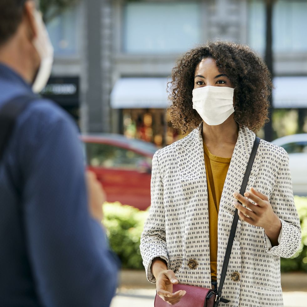 businesswoman wearing protective face mask talking to male coworker during covid9 pandemic in city