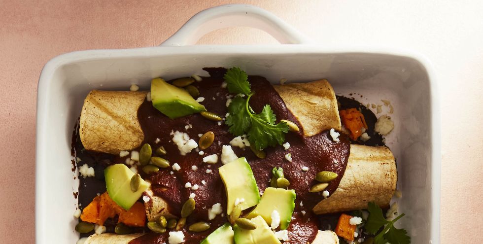butternut mole enchiladas with avocado on top in a white baking dish