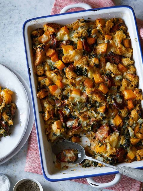 butternut squash andouille and herb stuffing in a white rectangle baking dish with blue trim and a spoon for serving