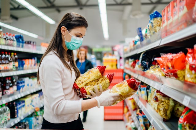 Buyer wearing a protective mask.Shopping during the pandemic quarantine.Nonperishable smart purchased household pantry groceries preparation.Woman buying few pasta packages.Budget pastas and noodles.