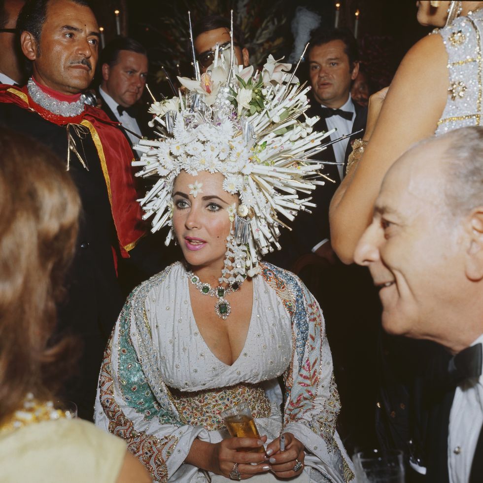 september 1967  english movie star elizabeth taylor attends a social function wearing an elaborate headdress of pearls and fake flowers, a jewelled dress and an emerald necklace  photo by keystonegetty images