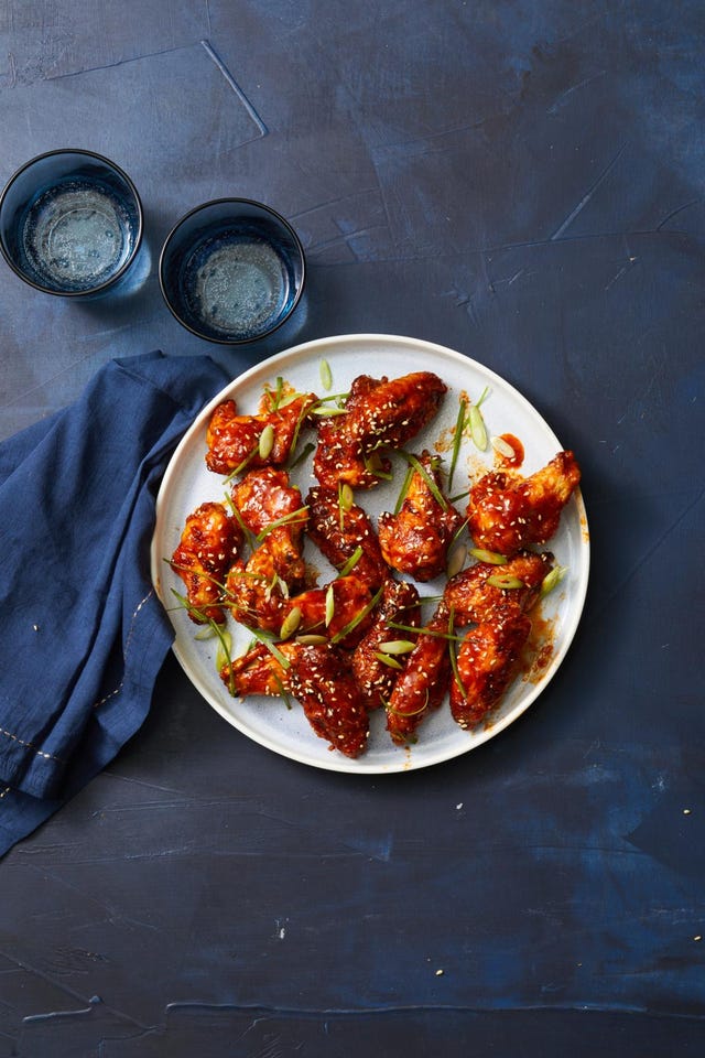 plate of glazed chicken wings garnished with sliced green onions and sesame seeds accompanied by two blue glasses