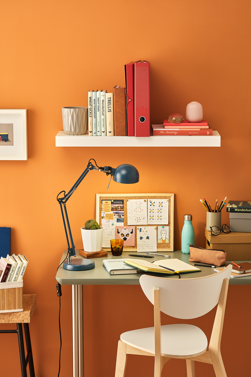 student with desk, chair and shelf messy table with notebooks, stationery, lamp and pinboard bright orange wall