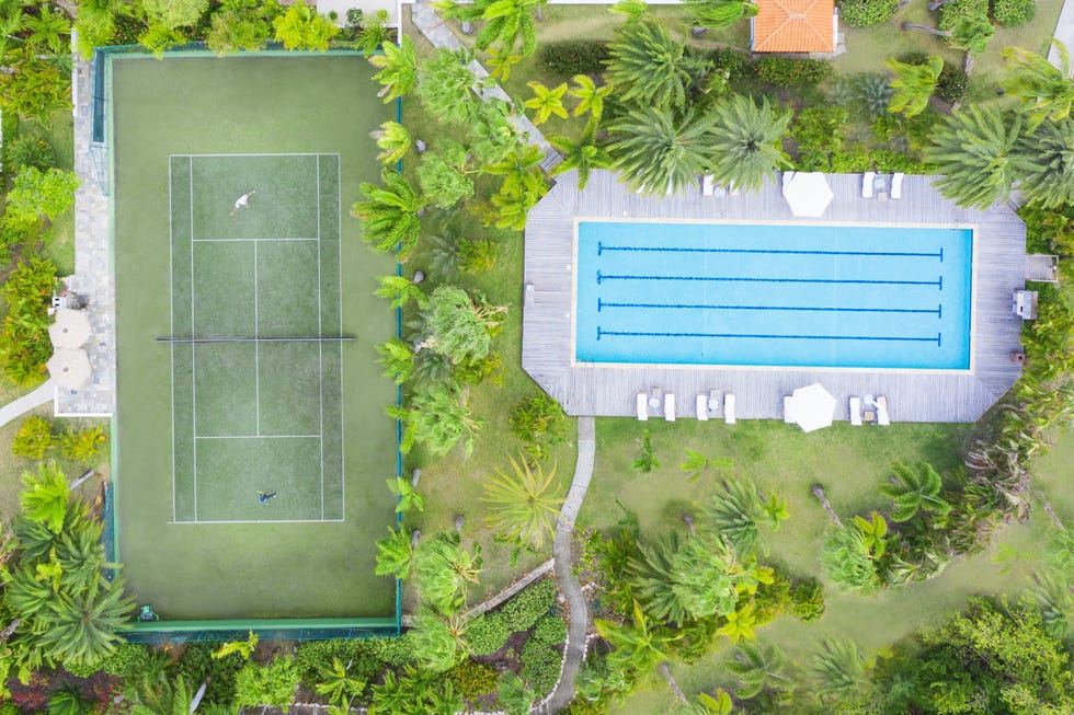 A recreational area featuring a tennis court and a swimming pool surrounded by palm trees.