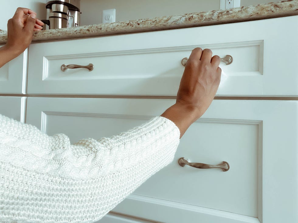 close up of unrecognizable woman in kitchen cleaning cabinet hardware with disinfectant wipe