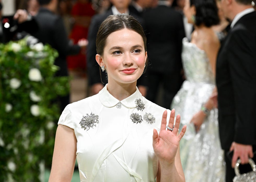 cailee spaeny wearing a white dress with silver accessories and waving with her left hand