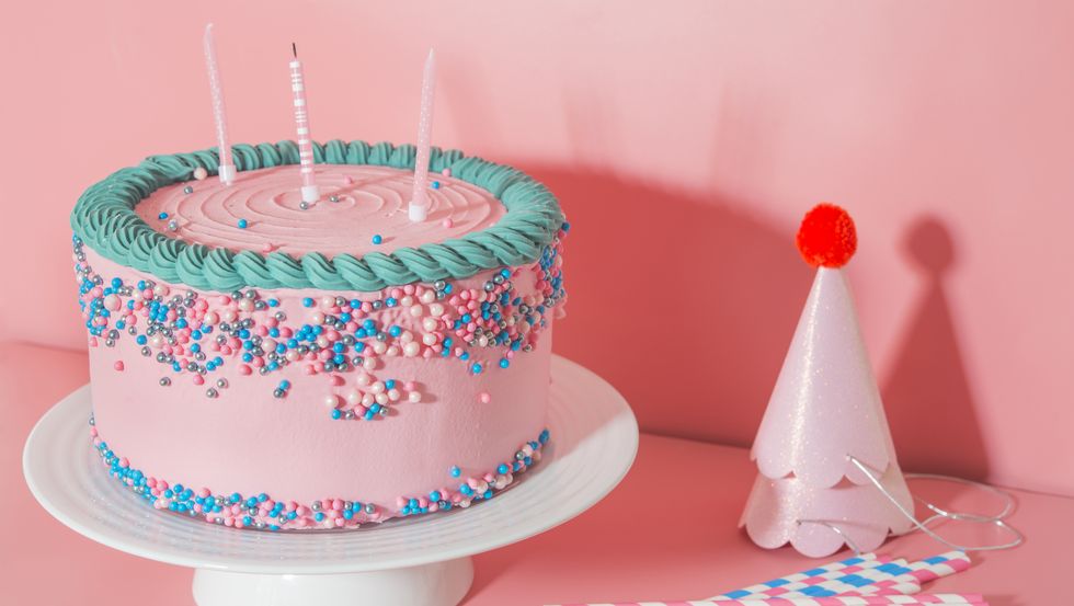 cake stand with strawberry birthday cake, drinking straws and party hats