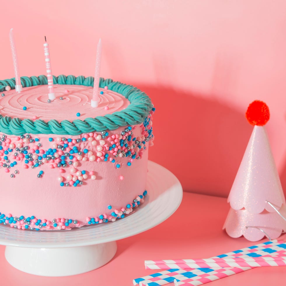 cake stand with strawberry birthday cake, drinking straws and party hats