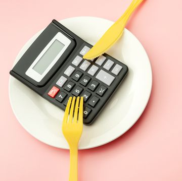 calculate expensive food spending costs, counting calories and weight loss program concept with calculator on empty plate, yellow fork and knife isolated on pink background with copy space