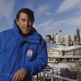 man in a snow jacket posing in front of a stadium and city skyline