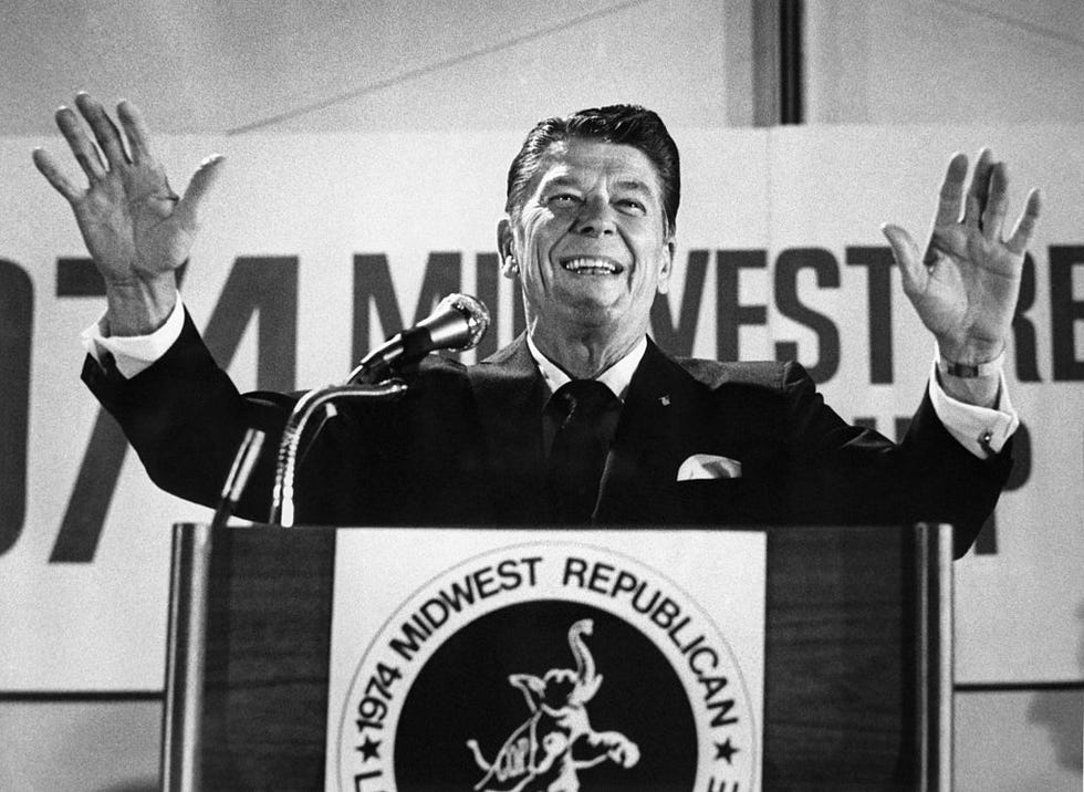 ronald reagan smiling and holding his hands in the air as he stands behind a podium speaking