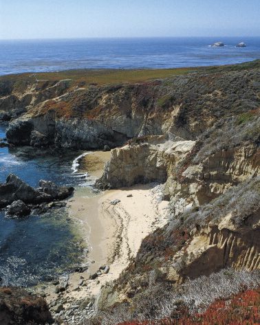 californian coast from overhead with beach surrounded by rocky, rugged landscape