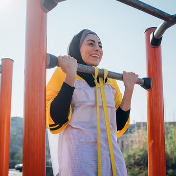 calisthenics at outdoor gym, young woman doing pull up on exercise equipment
