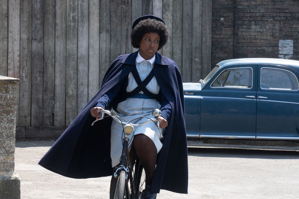 Renee Bailey fährt Fahrrad in einer Retro-Krankenschwesteruniform als Joyce Highland in „Ruf die Hebamme“, Staffel 13
