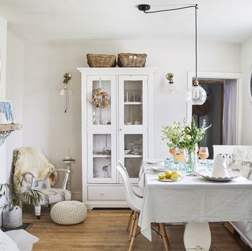 a dining room painted in an off white decorated with vintage pieces such as a hungarian bench, glass fronted cabinet and armchair upholstered in a pineapple fabric