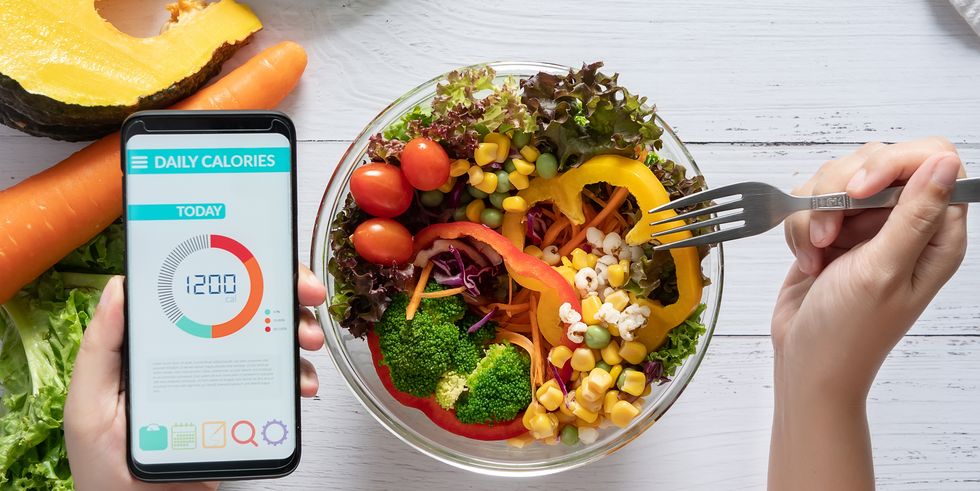 calories counting , diet , food control and weight loss concept calorie counter application on smartphone screen at dining table with salad, fruit juice, bread and fresh vegetable healthy eating
