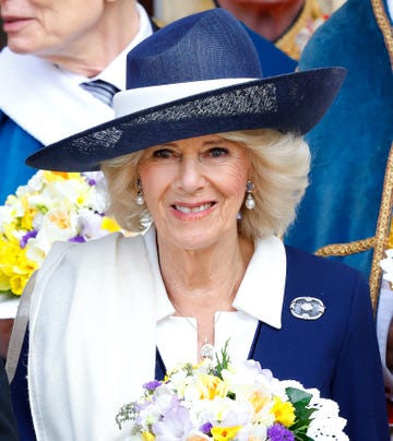 camilla who is now to be known as the queen pictured in a navy hat holding a bunch of flowers