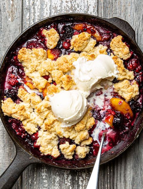 berry peach cobbler in a black cast iron skillet topped with vanilla ice cream