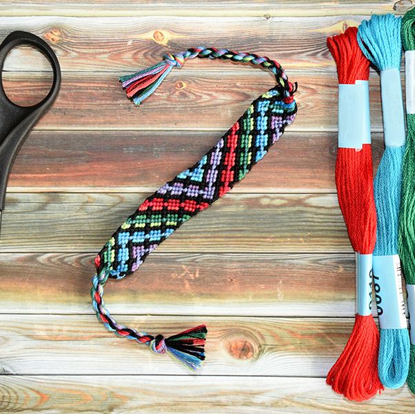woven diy friendship bracelet with abstract pattern near skeins of embroidery floss, scissors on wooden background friendship bracelets are a good housekeeping pick for best camping activites