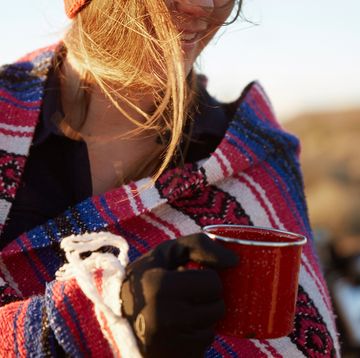 woman wrapping in camping blanket holding mug