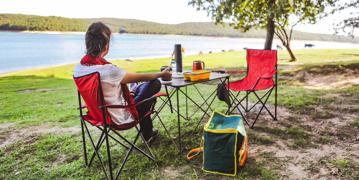 woman sitting in red camping chair in front of folding table next to lake