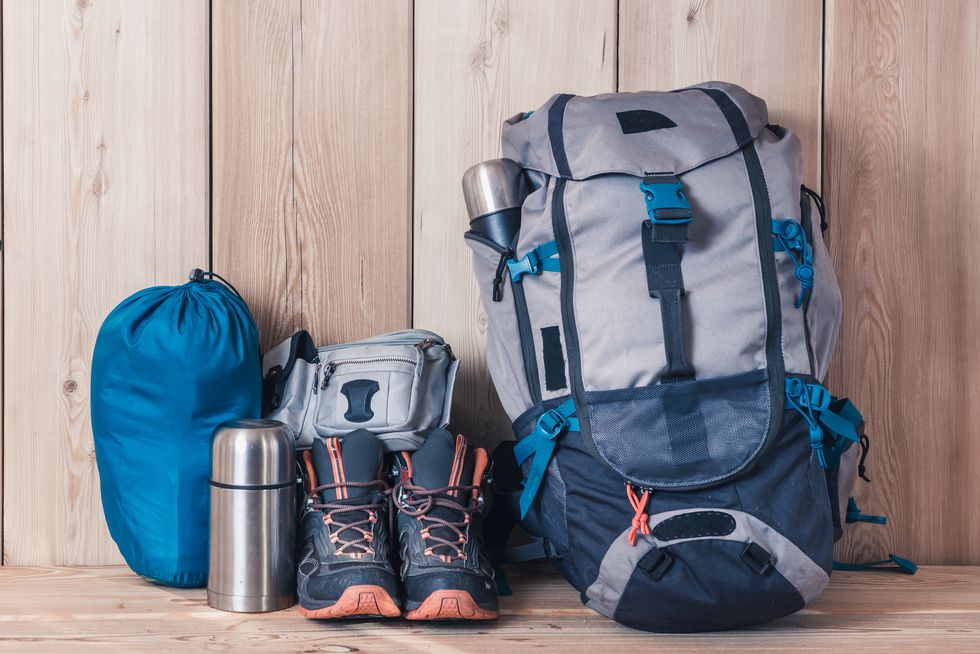 camping equipment, shoes, a backpack and a thermos on a wood background