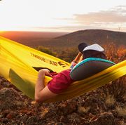 man drinking a beer in a hammock at sunset lying on teal and black camping pillow
