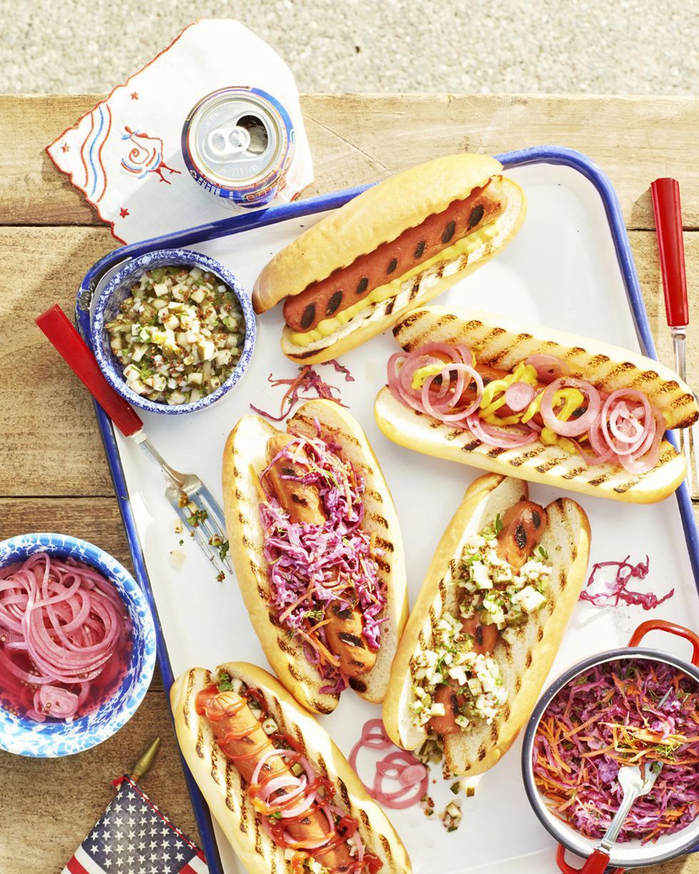 grilled hot dogs with various toppings arranged on a white tray with blue trim