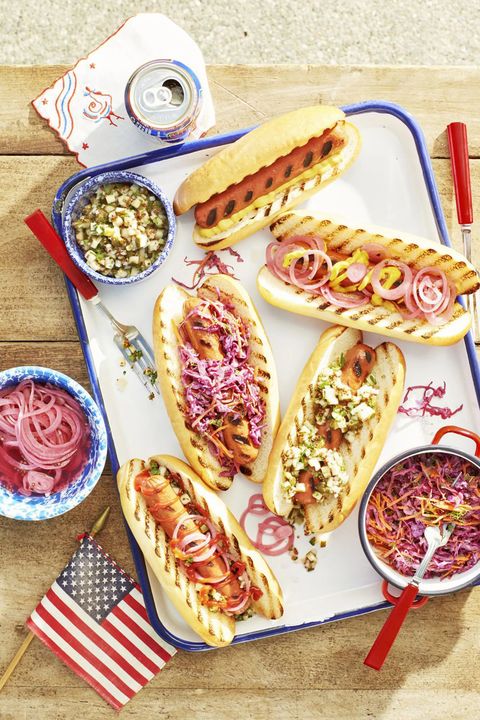 grilled hot dogs with various toppings arranged on a white tray with blue trim